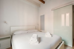 A hotel room with a bed, two bedside tables, a nightstand, a mirror, and a door.