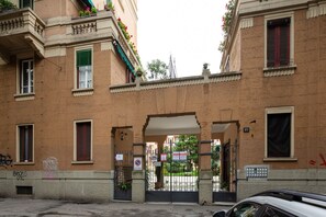 Un edificio con entrada protegida por un portón, varias ventanas y balcones con plantas.