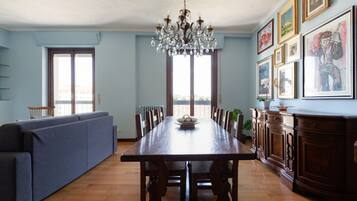 Uma sala de jantar com uma mesa de madeira, cadeiras, um candelabro, um sofá azul e um armário com quadros.