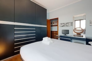 Ein modernes Hotelzimmer mit einem großen Bett, einem Schreibtisch mit Computer, einem Fernseher und einem Spiegel.