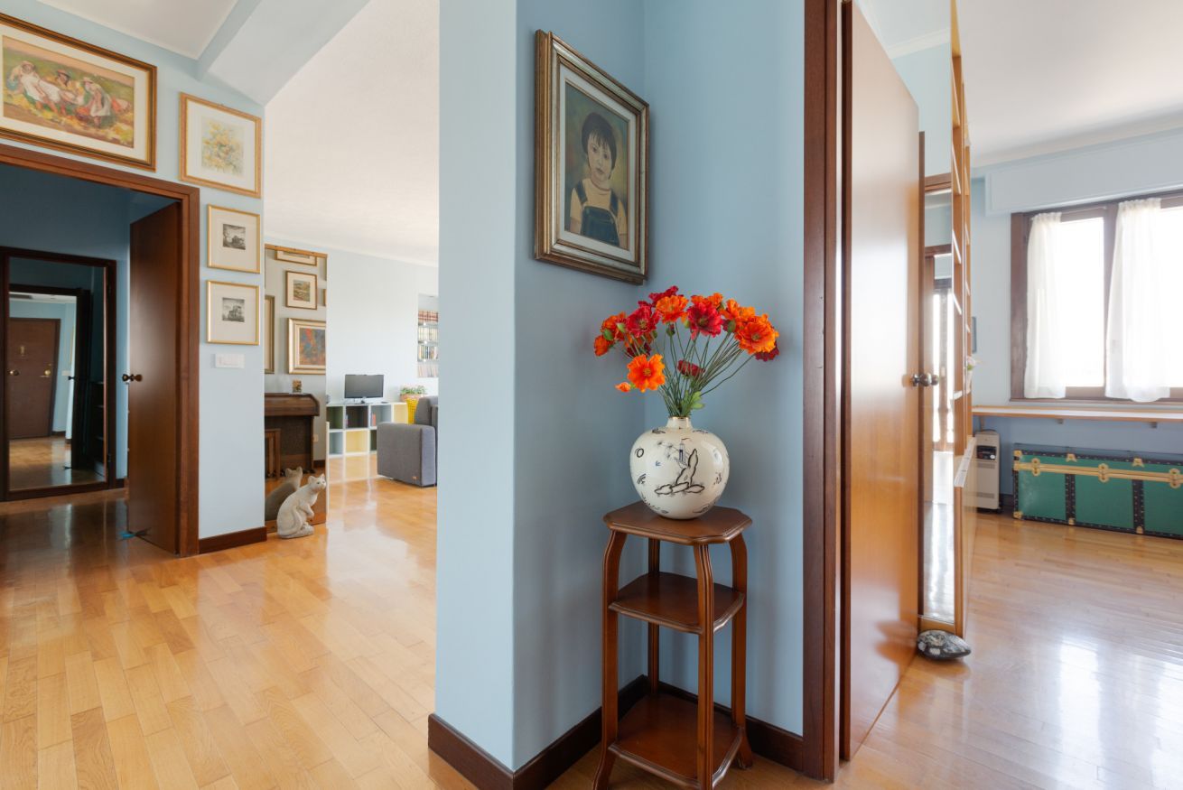 A room with a wooden floor, a vase with flowers, and framed pictures on the wall.