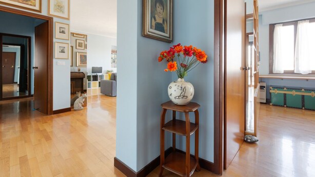 Una habitación con piso de madera, un jarrón con flores y cuadros en la pared.