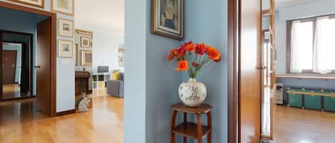 A room with a wooden floor, a vase with flowers, and framed pictures on the wall.