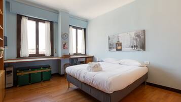 Quarto com cama, escrivaninha, cadeira, janela com cortinas, relógio de parede, quadro emoldurado e um baú verde.