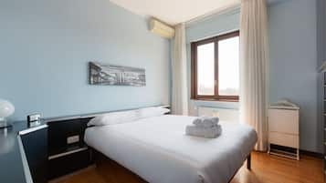 Una camera da letto con un letto, un comodino, un condizionatore d'aria a muro, una finestra con tende e un termosifone.