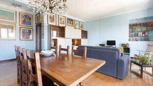 Un comedor con una mesa y sillas de madera, una araña y un sofá azul al fondo.