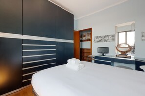 Een moderne hotelkamer met een groot bed, een bureau met een computer, een televisie en een spiegel.