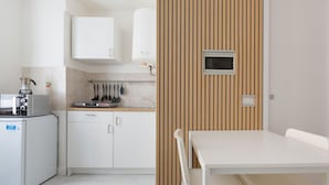 A compact kitchen with a microwave, coffee maker, and a small refrigerator. There is a wooden panel wall and a white table with chairs.