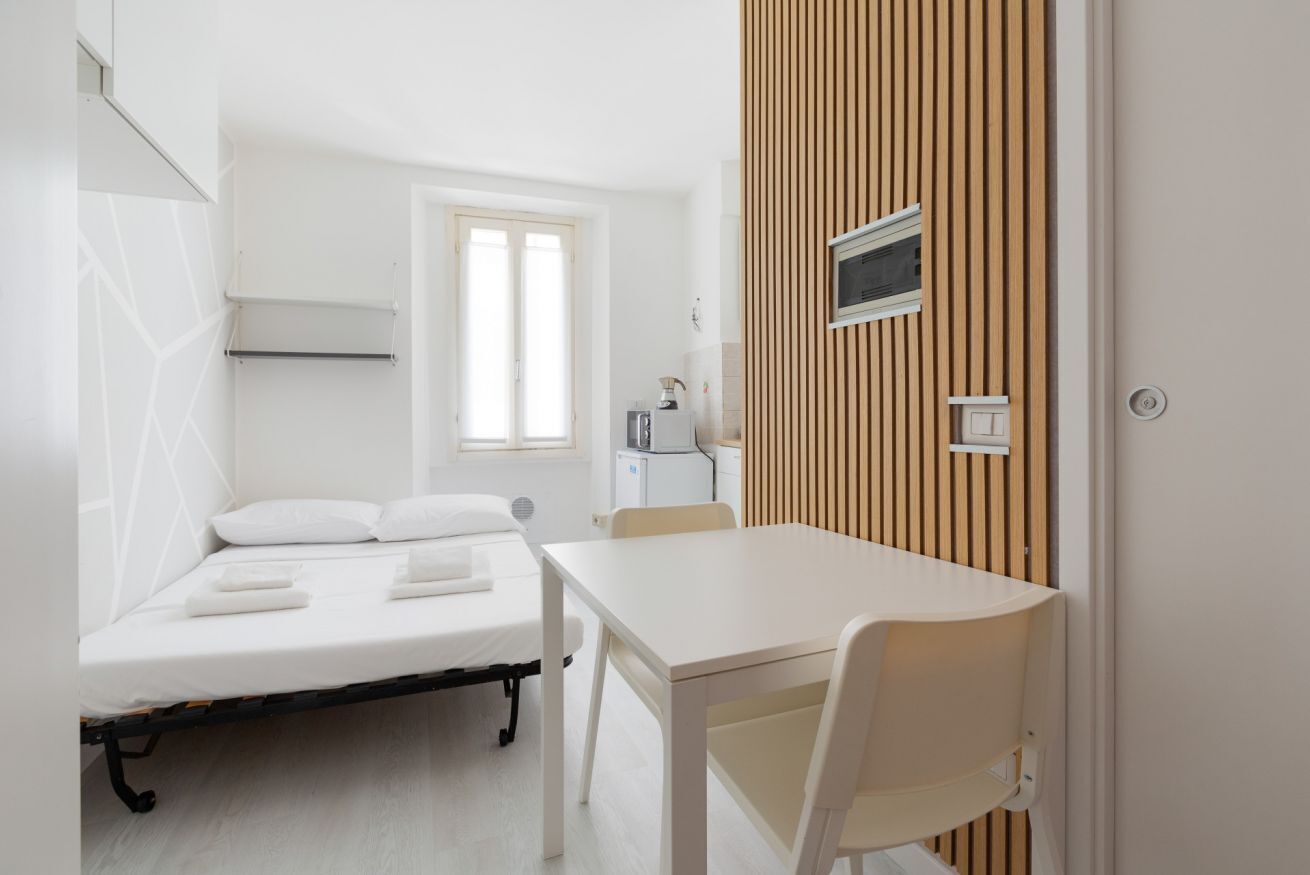 Une pièce avec un lit, une table et une chaise. Il y a une fenêtre et une porte.