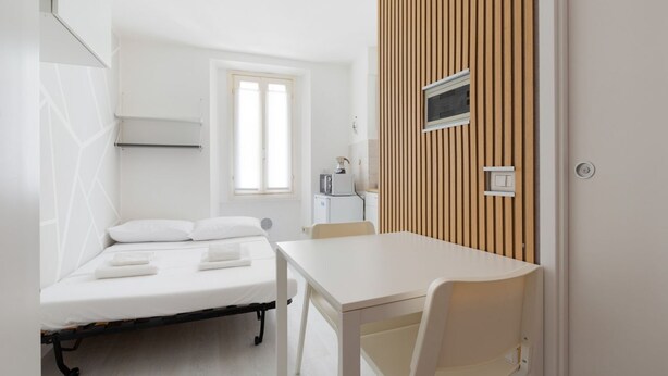 A room with a bed, a table, and a chair. There is a window and a door.
