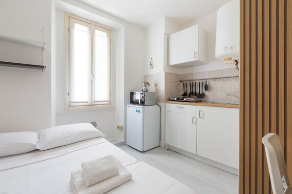 A compact hotel room with a bed, a small kitchenette, and a window.
