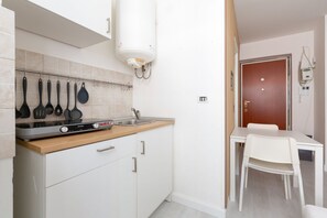A compact kitchen with a stove, sink, and white cabinets.
