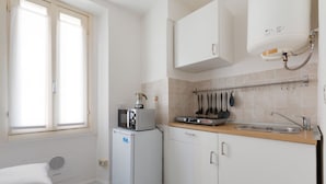 A compact kitchen with a microwave, a small refrigerator, a sink, and a window with blinds.