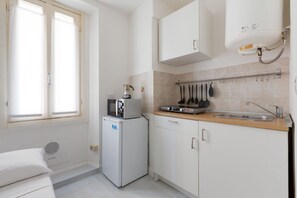 Una cocina compacta con microondas, un refrigerador pequeño, un lavamanos y una ventana con persianas.