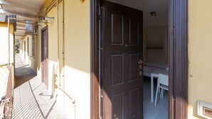 A narrow hallway with a door leading to a room with a bed and a small table.