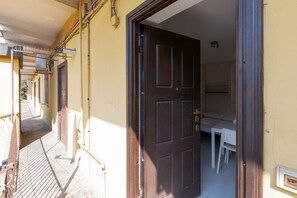 A narrow hallway with a door leading to a room with a bed and a small table.