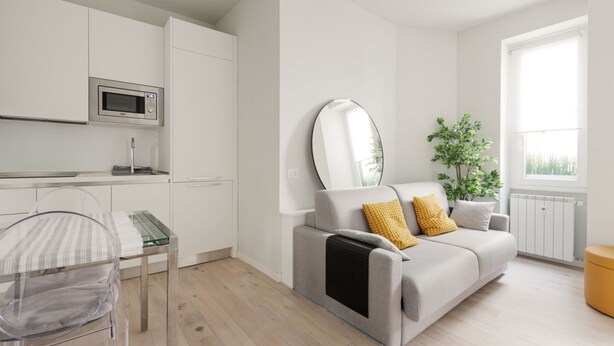 Ein modernes Apartment mit Küchenzeile, einer Couch mit Kissen, einem Spiegel und einem Fenster mit Aussicht.
