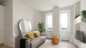 Ein modernes Wohnzimmer mit einer Couch, einem runden Spiegel, einer Topfpflanze, einem Fernseher und einem Fenster.
