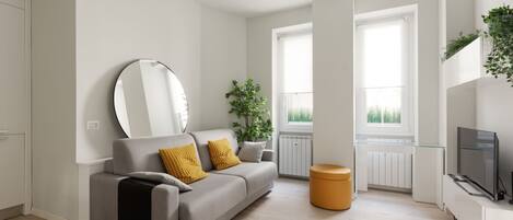 A modern living room with a sofa, a round mirror, a potted plant, a television, and a window.