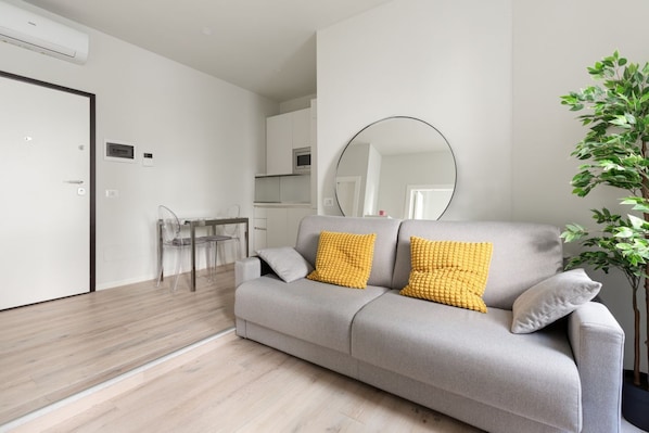 A modern living room with a grey sofa, a round mirror, and a potted plant.