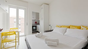 Hotellihuone, jossa on sänky, työpöytä tuoleineen, vaatekaappi ja näkymä ovesta.