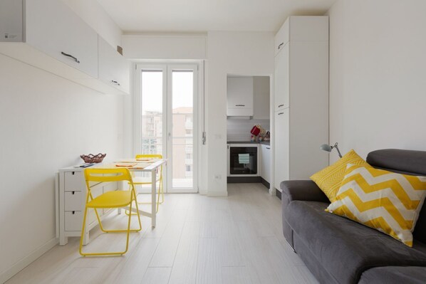 Un espacio habitable compacto con comedor, kitchenette y un sofá con cojines estampados.