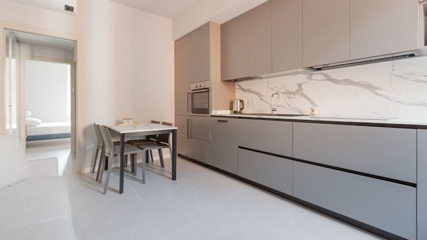 Une cuisine moderne avec des meubles gris, un plan de travail en marbre et un coin repas comprenant une table et des chaises.