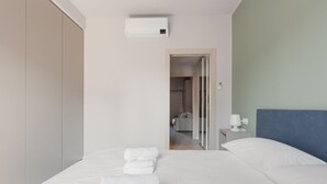Une chambre d’hôtel comprenant un lit, une table de chevet, une lampe, un appareil de climatisation et donnant sur la salle de bain.