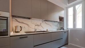 Une cuisine moderne dotée d’un plan de travail en marbre, d’appareils électroménagers en acier inoxydable et d’une fenêtre laissant entrer la lumière naturelle.