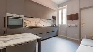 Une cuisine moderne dotée d’un four encastré, d’un plan de travail en marbre et d’un coin repas avec une table et des chaises.