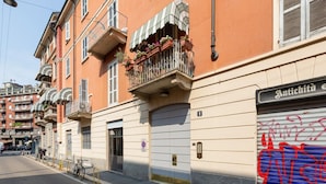 Un immeuble avec un balcon orné de fleurs, un magasin fermé dont la façade est recouverte de graffitis et un panneau indiquant qu’il est interdit de se garer.