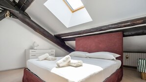 A bedroom with a sloped ceiling, a skylight, a bed with white linens, a white bedside table, and a red headboard. - GuestHost - Bright APT Milan Garibaldi & Moscova! (Milano)
