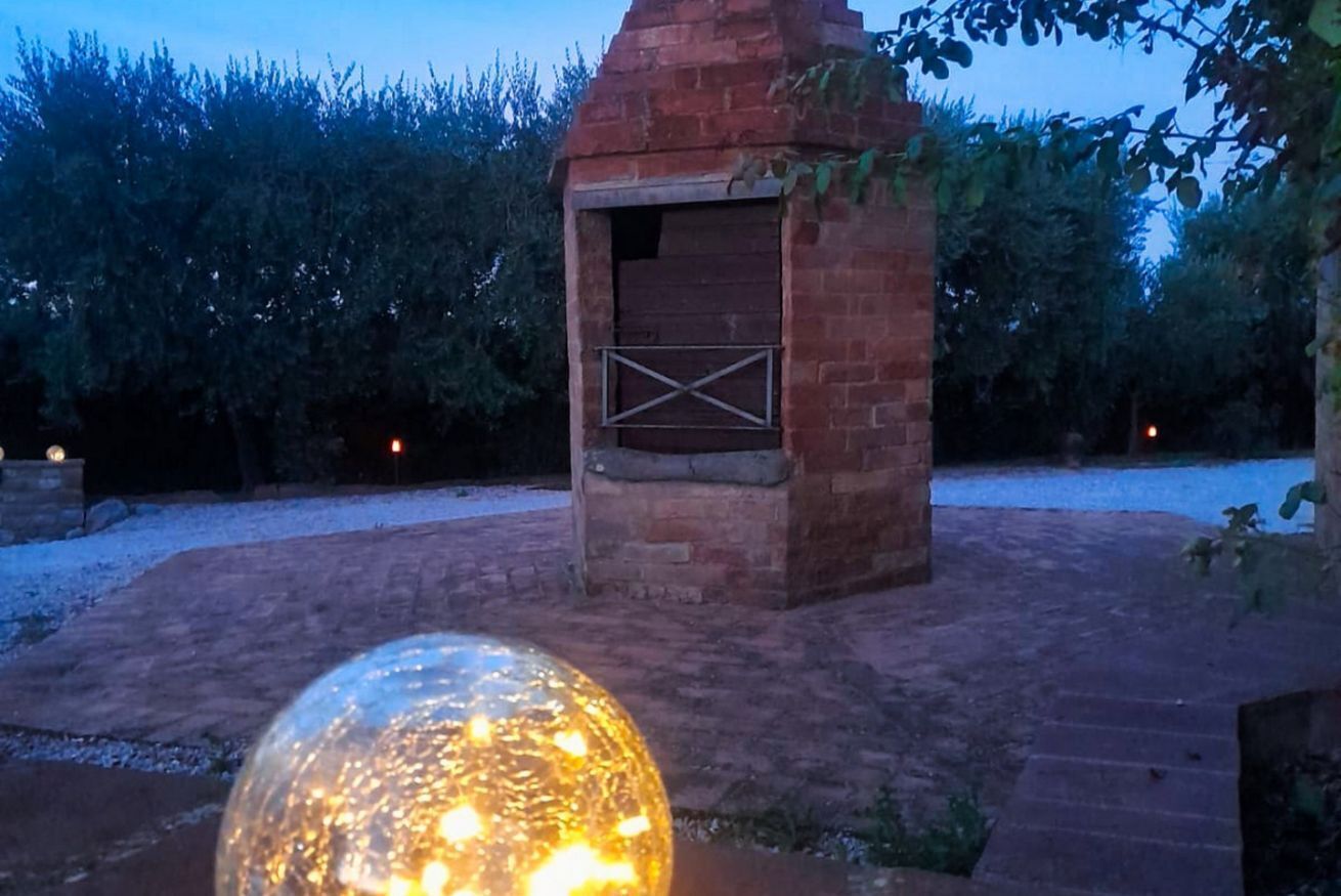 Construcció exterior de maó amb una porta de fusta, envoltada d'una zona pavimentada i vegetació.