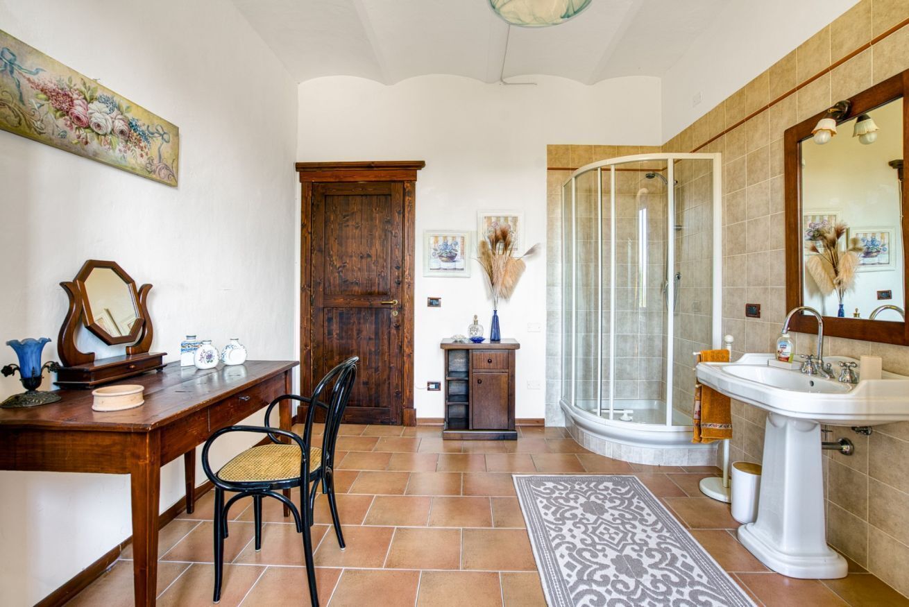 A bathroom with a shower, sink, and a wooden desk with a chair.