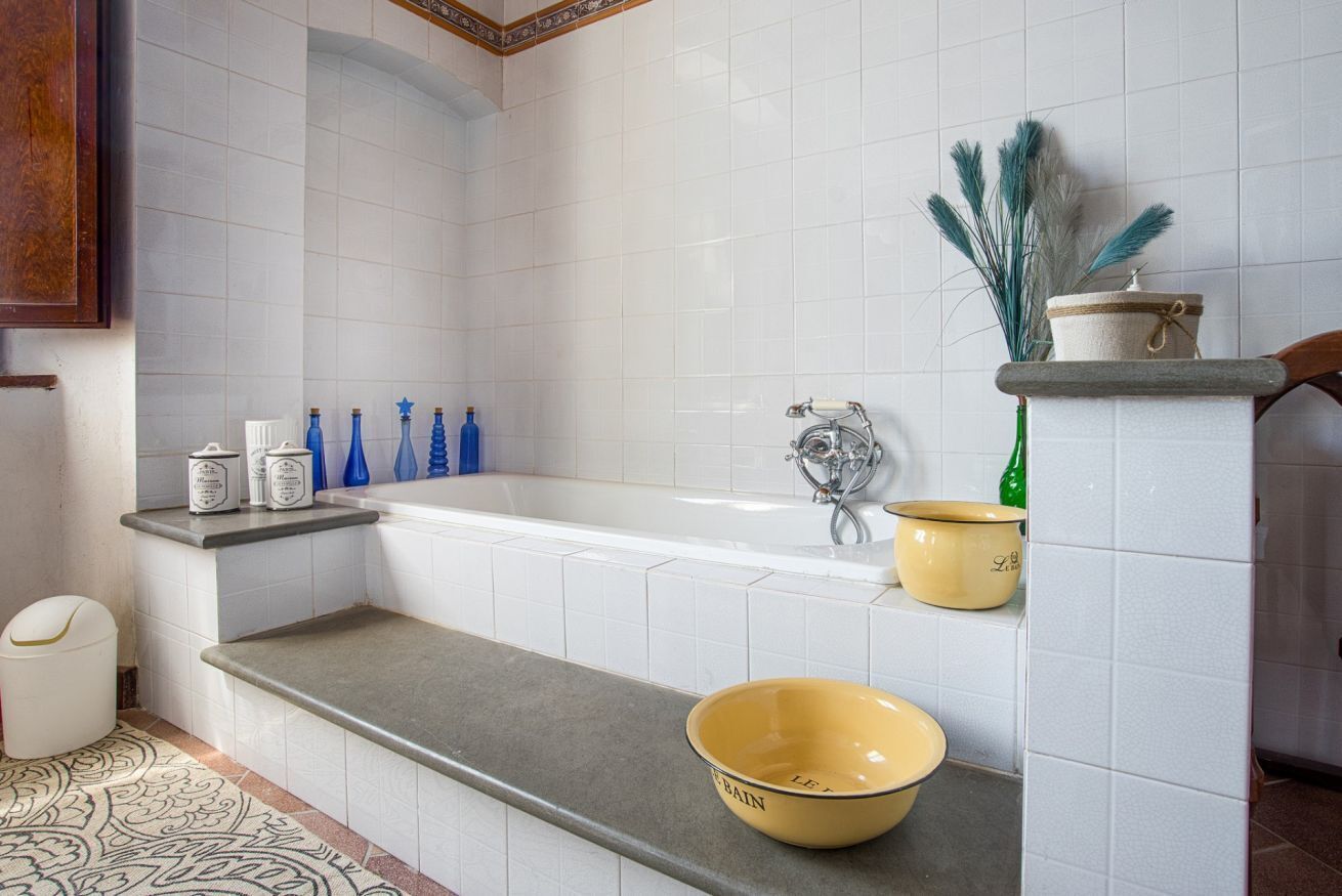 Ein Badezimmer mit weißen Fliesen, einer Badewanne, einem Waschbecken und einer Ablagefläche mit einer Schüssel.