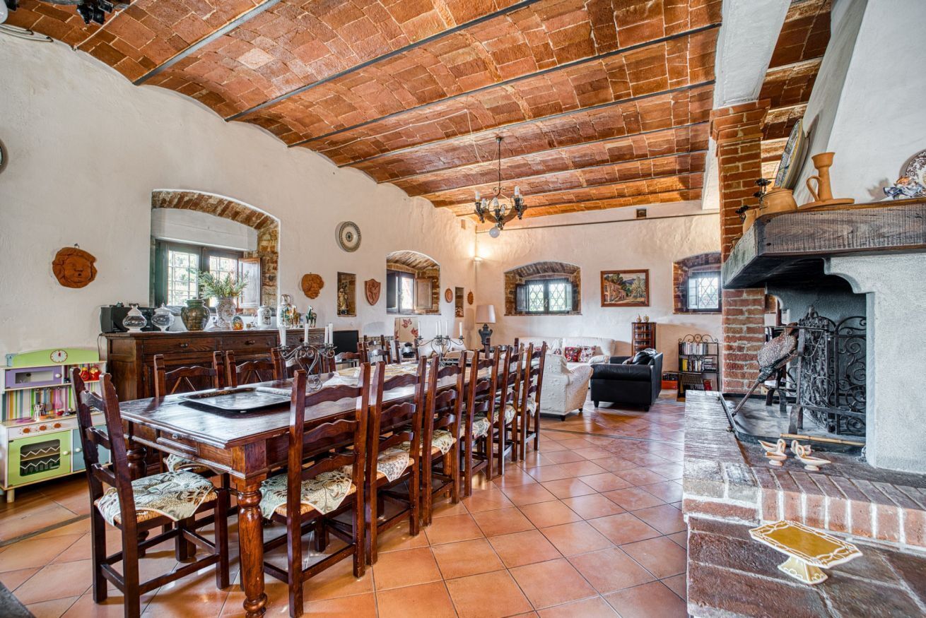A spacious dining area with a long wooden table and chairs, a fireplace, and a kitchen in the background.