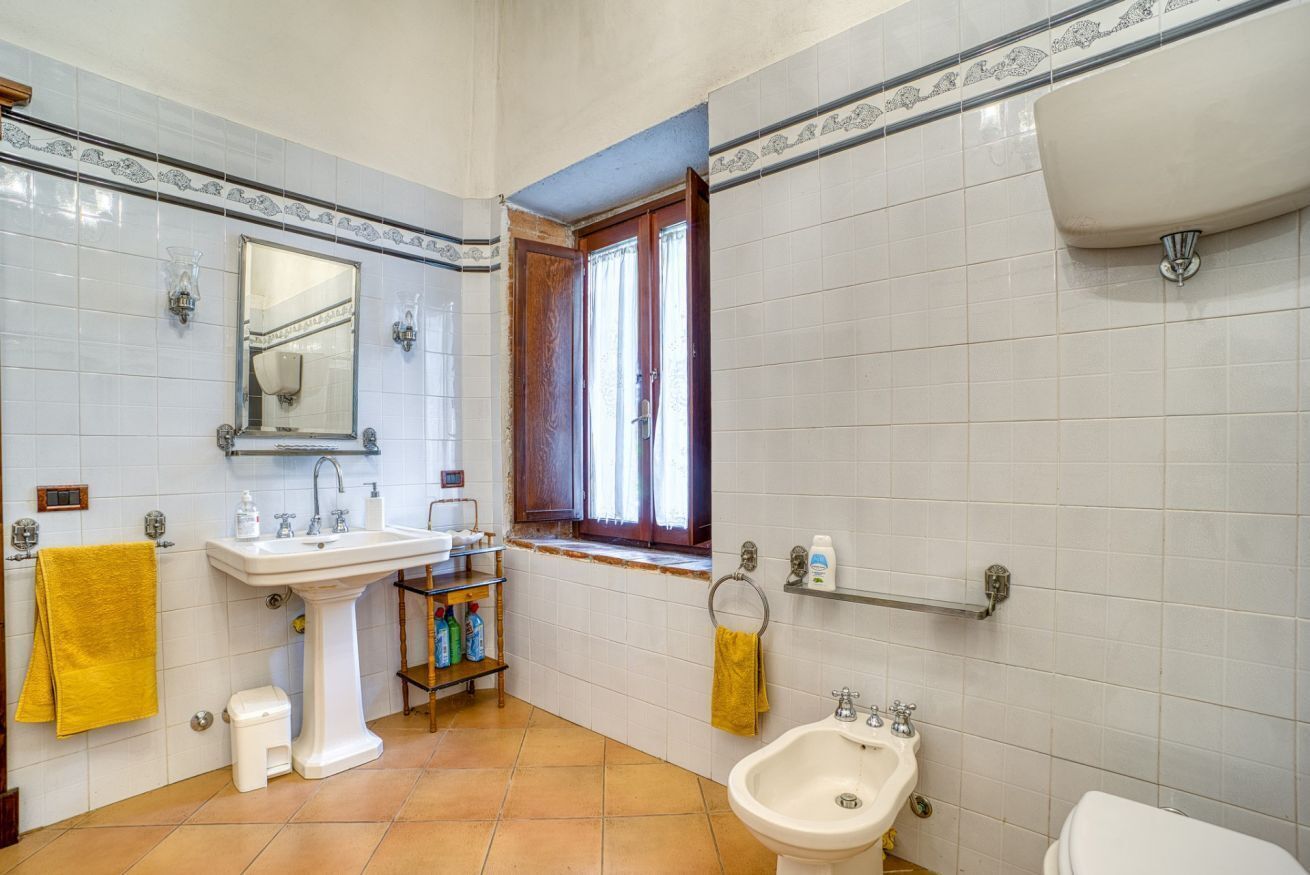 A bathroom with a pedestal sink, a bidet, a toilet, a mirror, and a window.