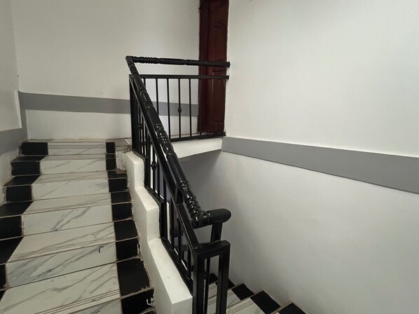 Un escalier aux carreaux noirs et blancs, une rambarde noire et une porte en bois.