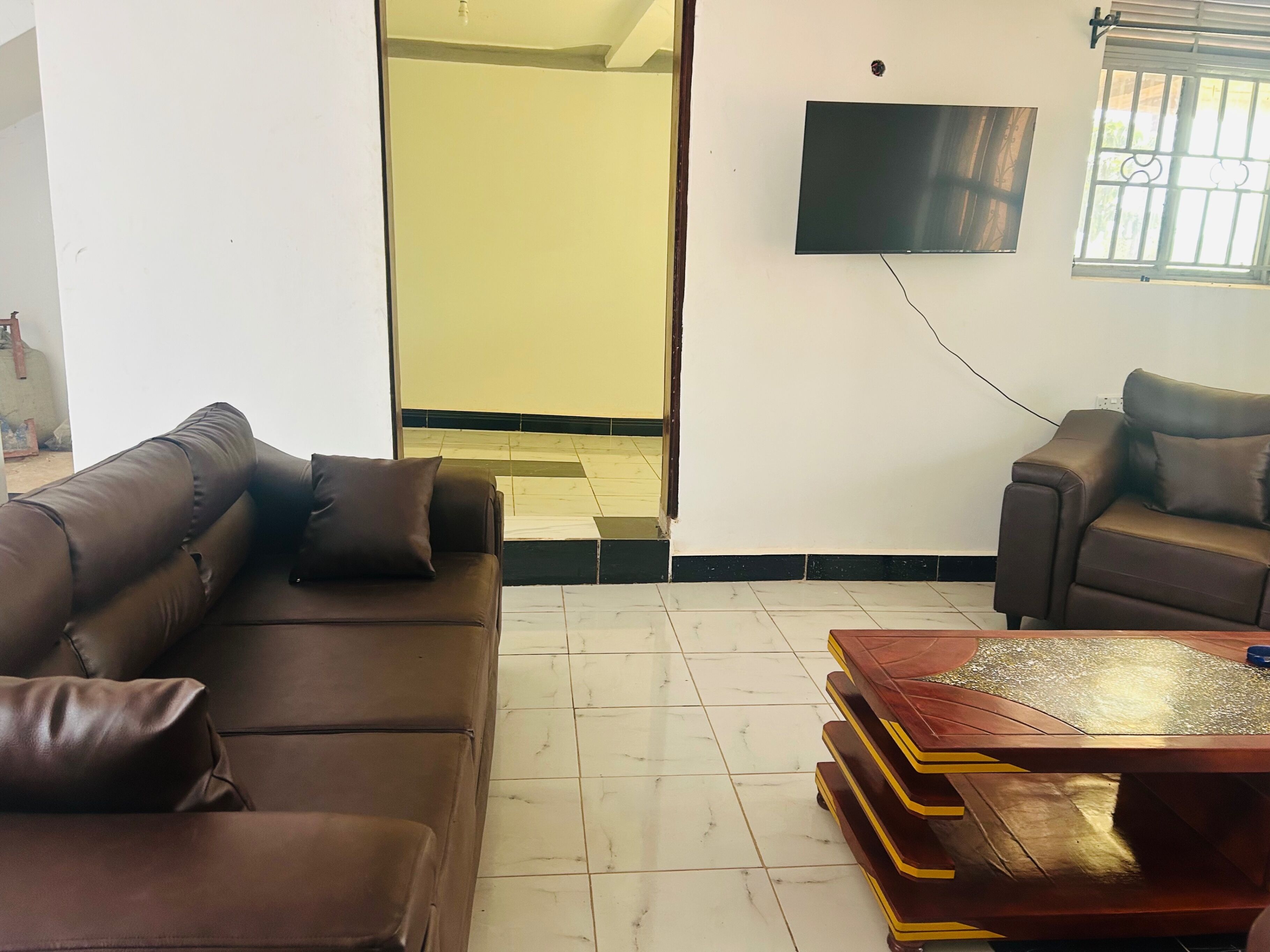 Una sala de estar con un sofá de cuero marrón, un sillón de cuero marrón, una mesa de centro de madera y un televisor de pantalla plana montado en la pared.