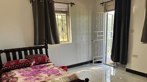 A bedroom with a bed, curtains, a window with a view, and a door leading outside.