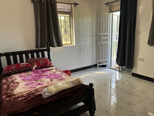 Une chambre à coucher avec un lit, des rideaux, une fenêtre donnant sur un paysage agréable et une porte menant à l’extérieur.