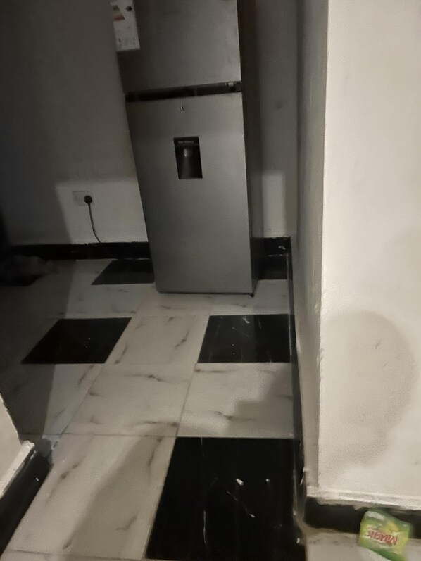 Eine Küche mit Kühlschrank, gefliestem Boden und einer Steckdose.