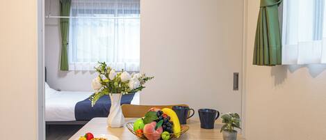 Una habitación de hotel con una cama, una mesa de comedor con alimentos para el desayuno, un florero con flores y vistas de la habitación a través de una ventana.