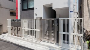 A modern building with a gated entrance, a visible staircase, and a sign indicating the building number. - LIVION V Hatagaya by Tranova (Tokyo)