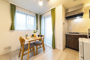 A compact kitchen with a stove, a small refrigerator, and a dining area with a table and chairs. - LIVION V Hatagaya by Tranova (Tokyo)