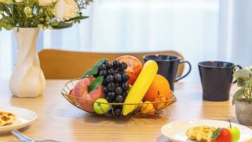 A dining table with a fruit basket, a vase with flowers, and a coffee mug.