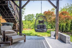 A covered outdoor seating area with a swing chair, a wicker sofa, and a concrete floor.