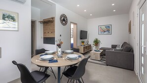 Una sala moderna con un sofá gris, una mesa de comedor de madera con sillas, un televisor y un reloj en la pared.