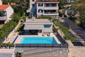 Un edificio moderno de dos pisos con piscina en la azotea, paneles solares y fachada de piedra.