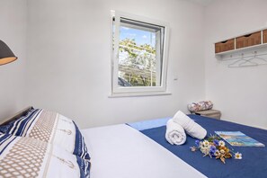 A bedroom with a bed, a window, a bedside table, and a hanging shelf.